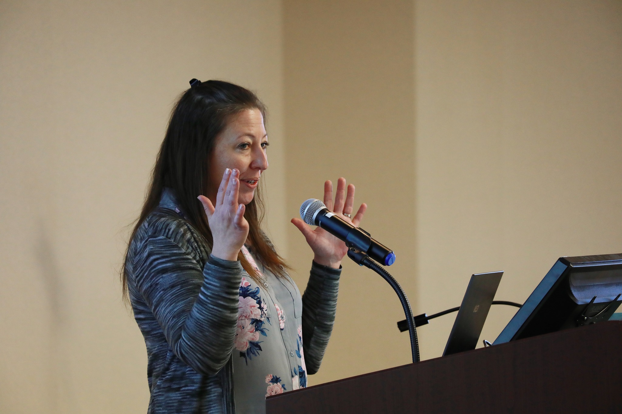 Laura Baskall Smith speaks passionately at a podium during a presentation on Childhood Apraxia of Speech.